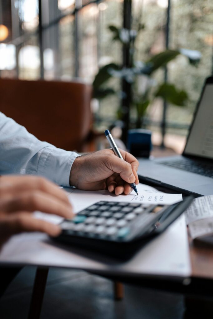 Free A person calculating finances with a calculator and pen on a desk indoors. Stock Photo